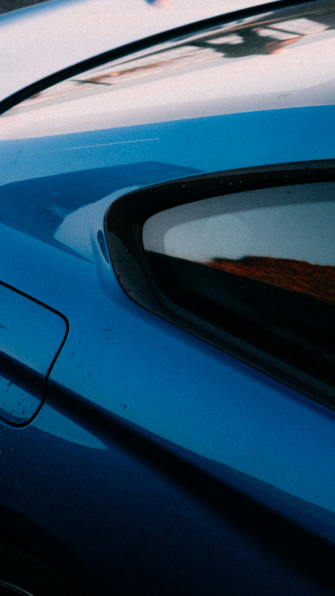 Close-up detail shot of a glossy blue car body panel with a black window trim and a small reflection in the glass.