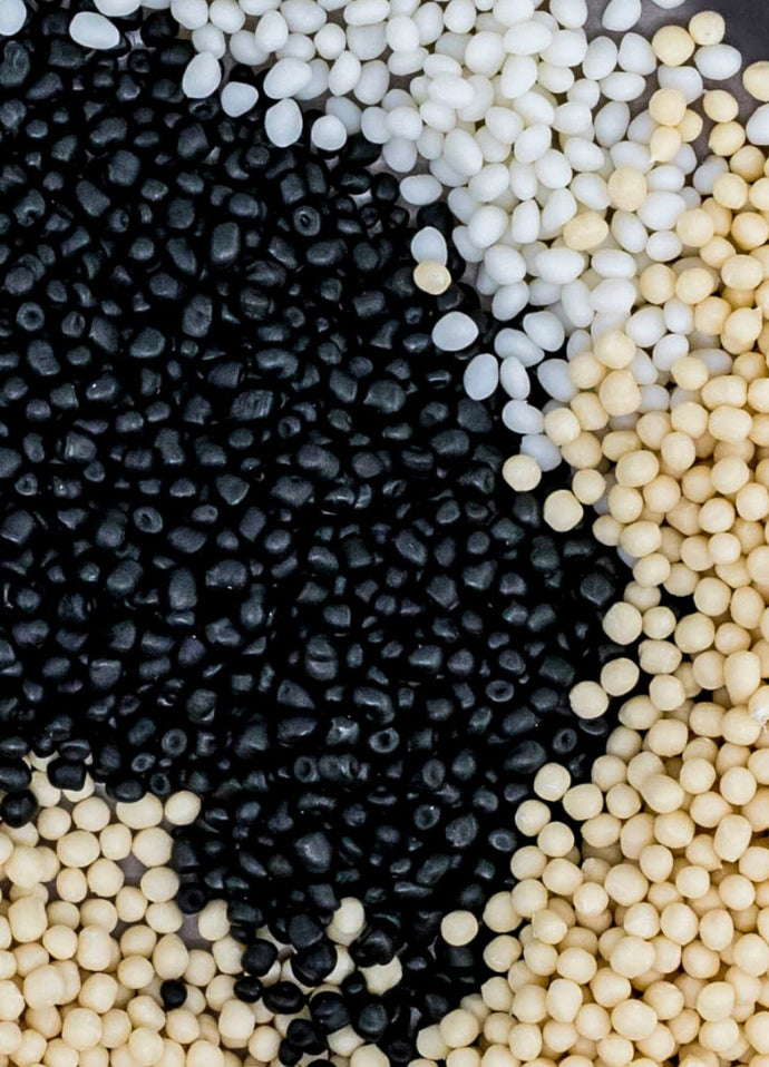 Thermoplastic elastomer pellets in black, white and natural colors, showing raw polymer material variations used in elastomer processing.