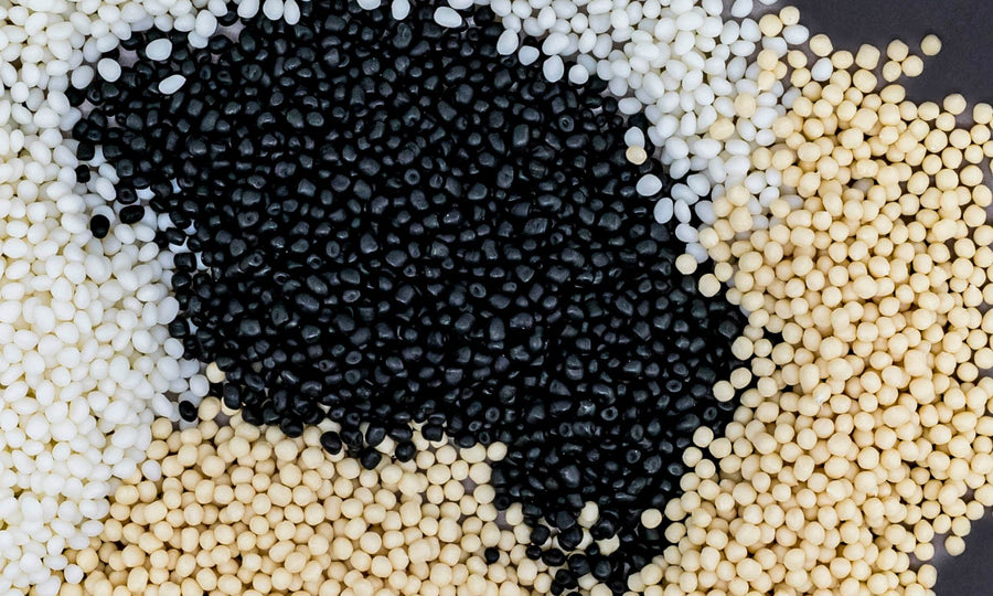 Thermoplastic elastomer pellets in black, white and natural colors, showing raw polymer material variations used in elastomer processing.